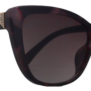 Könnte beinhalten: Eine Sonnenbrille im Cat-Eye-Stil aus Schildpatt mit schwarzen Bügeln und einem goldenen Akzent am Bügel.