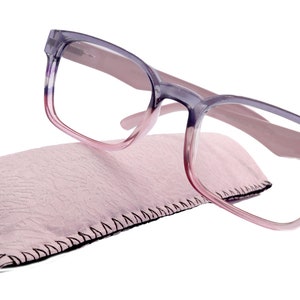 Könnte beinhalten: Eine Brille mit lila und rosa Farbverlauf und einem rosa Mikrofaser-Reinigungstuch.