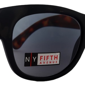 Puede incluir: Gafas de sol negras de ojo de gato con un patrón de caparazón de tortuga en las patillas. Las gafas tienen lentes grises oscuras y dicen "NY FIFTH AVENUE" en el marco.