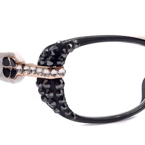 Puede incluir: Gafas negras y blancas con pedrería en las patillas. Las monturas son de forma ovalada y tienen un patrón blanco en las patillas.