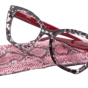 Könnte beinhalten: Cat-Eye-Lesebrille mit einem Schildpatt-Gestell und roten Bügeln. Die Brille liegt auf einem pinkfarbenen und schwarzen Etui mit Schlangenhautmuster.