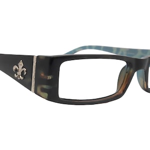 以下が含まれることがあります： 黒い長方形の眼鏡。テンプルにはフルール・ド・リスのエンブレムが付いています。フレームはべっ甲柄で、テンプルには青色のアクセントがあります。レンズはクリアです。