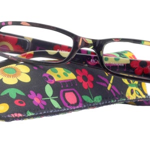 Può includere: Occhiali da lettura neri con custodia a stampa floreale e coccinella colorata. La custodia ha una chiusura a zip e gli occhiali hanno una montatura nera.