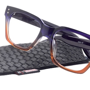 Könnte beinhalten: Violette und orangefarbene, quadratische Brillen mit Ombre-Effekt in einem schwarzen gewebten Etui. Das Etui hat ein rotes und weißes Etikett mit dem Text "NY" darauf.