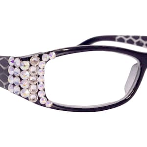 May include: Black eyeglasses with a geometric pattern on the arms and clear lenses. The frames are decorated with a row of clear rhinestones.