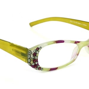 May include: Green and purple patterned reading glasses with rhinestones on the temples. The glasses have a clear lens.