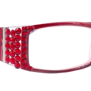 Puede incluir: Gafas rojas con lentes transparentes y un adorno de cristal en el lateral. La montura tiene un diseño de flor de lis.