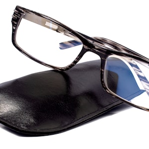 Puede incluir: Gafas de lectura grises con una funda de cuero negro. Las gafas tienen una graduación de +2,75.