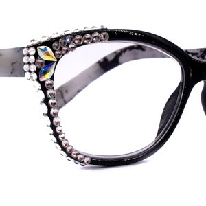 Könnte beinhalten: Schwarze Cat-Eye-Brille mit klaren Gläsern und einem marmornen Bügel. Die Rahmen sind mit Strasssteinen an den Rändern verziert.