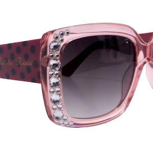 May include: Pink sunglasses with a black and red polka dot pattern on the arms and rhinestones around the frames. The sunglasses say "Petite Rose" on the arm.