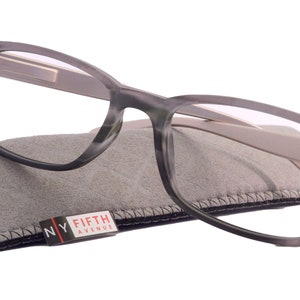 Könnte beinhalten: Graue und weiße rechteckige Brille mit einem grauen Mikrofaser-Etui. Das Etui trägt den Schriftzug "NY FIFTH AVENUE".