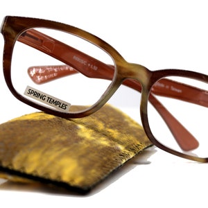 Puede incluir: Gafas de lectura de carey marrón con bisagras de resorte y una funda de microfibra marrón. Las gafas tienen una potencia de lente de +1,50 y un puente de 26 mm. El texto "SPRING TEMPLES" está impreso en la lente izquierda.