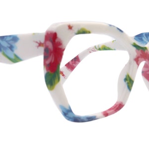 May include: White eyeglasses with a floral pattern featuring pink, blue, and green flowers. The frame is a unique geometric shape.
