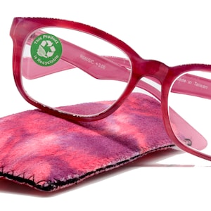 May include: Pink reading glasses with a +3.00 magnification and a pink and purple tie-dye microfiber cleaning cloth. The glasses are made of plastic and have a square shape. The cleaning cloth is made of soft microfiber and has a tie-dye pattern.