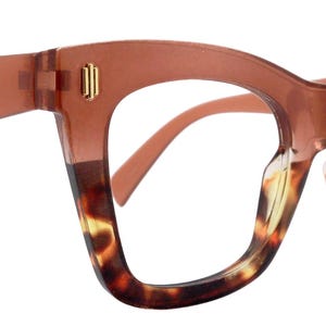 Könnte beinhalten: Braune und Schildpatt-Brille mit Cat-Eye-Form. Die Fassungen haben einen Farbverlauf, der von einem soliden Braun zu einem Schildpattmuster übergeht. Goldfarbene Akzente sind an den Bügeln zu sehen.