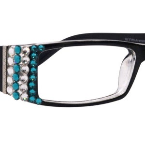 Puede incluir: Gafas de pasta negra con pedrería turquesa y transparente en el lateral de la montura. La montura tiene un diseño de flor de lis en el lateral.