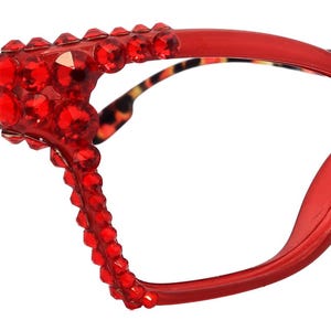 Peut inclure: Lunettes rouges en forme d'œil de chat avec des strass. Les montures sont d'un rouge vif, et les branches présentent un motif léopard. Les strass sont regroupés sur les bords extérieurs des montures.