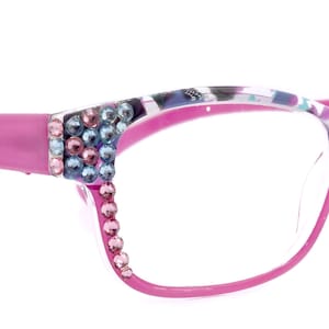 May include: Pink eyeglasses with a colourful, patterned frame and rhinestones around the lenses.