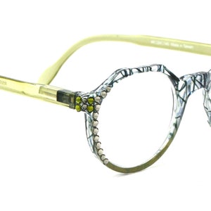 May include: A pair of round, clear-lens glasses with a black and white patterned frame. The frame is decorated with small, white rhinestones and yellow accents.