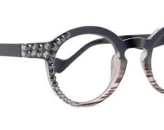Puede incluir: Gafas redondas negras con pedrería alrededor de las monturas y lentes con degradado rosa y blanco.