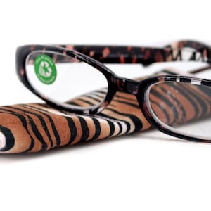 May include: Black and brown reading glasses with a tiger print frame and a matching tiger print case. The glasses have a +1.75 lens strength and a 22 mm lens size.