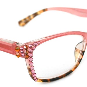 May include: Pink eyeglasses with a cat-eye frame. The frames are adorned with pink and orange rhinestones along the outer edges. The temples have a tortoiseshell pattern. The lenses are clear.