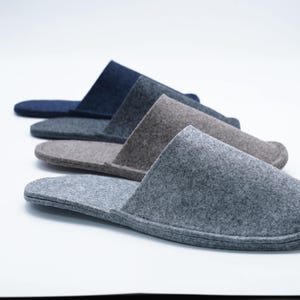 May include: Four pairs of felt slippers in different shades of gray, blue, and brown. The slippers are laid out in a row, with the darkest color at the top and the lightest color at the bottom.