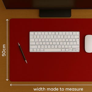 Puede incluir: Una alfombrilla de escritorio roja con un teclado, un ratón y un bolígrafo blancos. La alfombrilla mide 50 cm de altura y está hecha a medida para el ancho. El teclado está centrado.