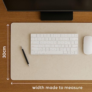 Könnte beinhalten: Eine beige rechteckige Schreibtischunterlage mit einer weißen Tastatur, Maus und einem schwarzen Stift. Die Unterlage ist 30 cm breit und trägt den Text "width made to measure". Das Setup befindet sich auf einem Holzschreibtisch.