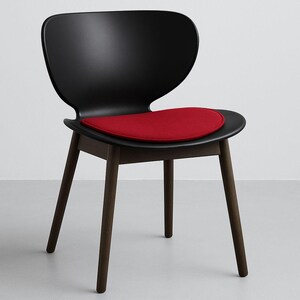 May include: A modern black chair with a curved back and a red seat cushion. The chair has four dark brown wooden legs. The seat cushion is a vibrant red color, providing a striking contrast to the black chair.