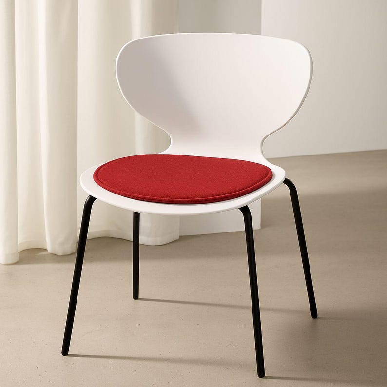 May include: A modern white chair with a curved back and a round, red seat cushion. The chair has four black metal legs. The design is minimalist and contemporary, suitable for various interior styles.