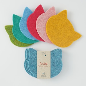 May include: A selection of cat-shaped felt coasters in shades of green, teal, blue, red, pink, and yellow. A package of blue coasters is also present, with the text "feltd. Feltdesign".