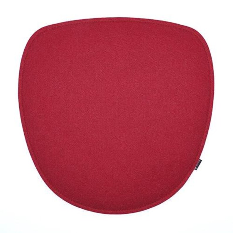 May include: A solid red, oval-shaped cushion with a textured surface. The cushion has a stitched border and a small black tag on the lower right corner. The cushion is designed for seating.