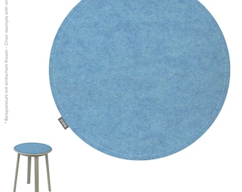 Puede incluir: Un cojín redondo de fieltro azul claro con costuras blancas en el borde. Se muestra junto a un taburete pequeño con un asiento azul a juego. El texto "feltd." es visible en el cojín. El color es azul coelin.