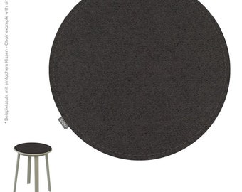 Puede incluir: Un cojín de silla redondo gris oscuro con un borde cosido, junto a una mesa pequeña con una tapa gris oscuro y patas plateadas. El cojín tiene el texto "feltd." en una pequeña etiqueta. El color es graphit.