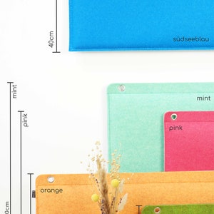 K&ouml;nnte beinhalten: Eine Auswahl an Filz-Organizern in verschiedenen Farben. Das gr&ouml;&szlig;te ist orange, 60 cm hoch, und das kleinste ist gr&uuml;n, 20 cm hoch. Weitere Farben sind Blau, Mint und Pink. Jeder Organizer hat eine Metall&ouml;se und gen&auml;hte Kanten.