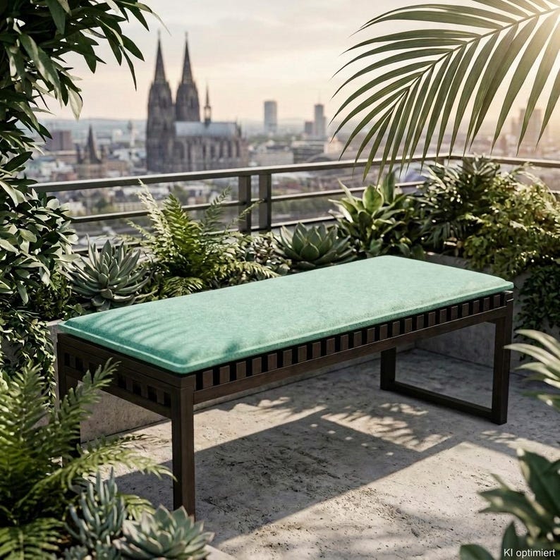 Maßgefertigte Bankauflage aus recyceltem PET-Filz (rPET) in Mintgrün auf einer dunklen Holzbank im begrünten Außenbereich mit Blick auf den Kölner Dom. Die passgenaue Filz Sitzauflage bietet angenehmen Sitzkomfort, schützt die Bankoberfläche und ist strapazierfähig, pflegeleicht und vegan. Individuell nach Maß gefertigt, in zahlreichen Farben und verschiedenen Polsterstärken erhältlich. Ideal für Sitzbänke auf Balkon, Terrasse, im Esszimmer oder in der Küche. Made in Cologne.