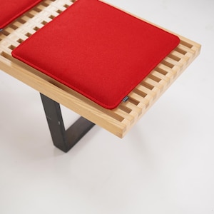 Peut inclure: Un banc en bois avec un design à lattes et deux coussins rouges. Le banc a des pieds en métal noir.