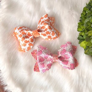 May include: Two fabric hair bows, one with an orange and white fish print and one with a pink and white cookie print.