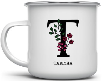 May include: White enamel mug with a black letter T decorated with green leaves and pink flowers. The name Tabitha is printed below the letter.