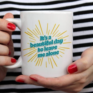 May include: White ceramic mug with a yellow and teal design. The mug has the text "It's a beautiful day to leave me alone".