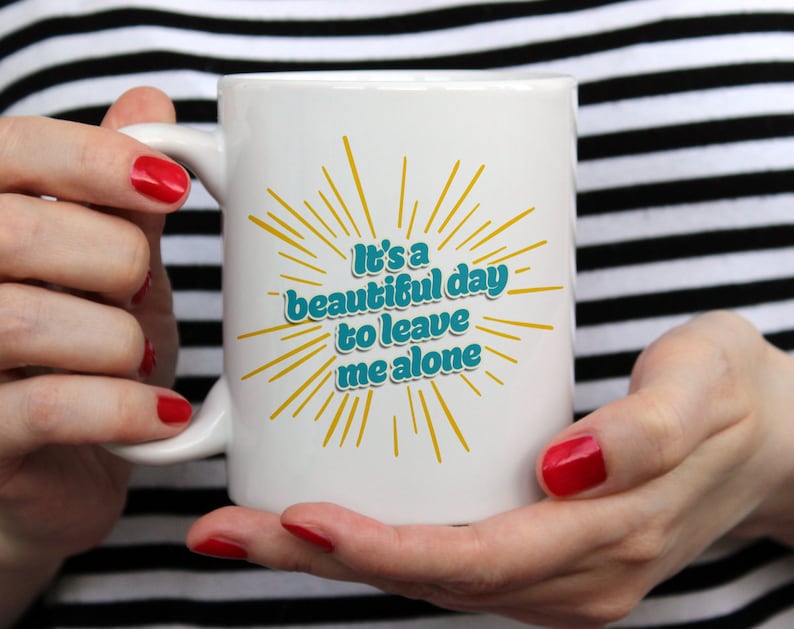 May include: White ceramic mug with a yellow and teal design. The mug has the text "It's a beautiful day to leave me alone".