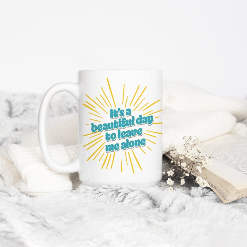 May include: White ceramic mug with a yellow and blue design. The mug has the text "It's a beautiful day to leave me alone".