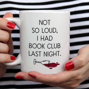 May include: White ceramic mug with black text that reads "Not so loud, I had book club last night." A black and white illustration of a wine glass with red wine spilled on the white surface.