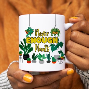 Puede incluir: Taza de cer&aacute;mica blanca con un dise&ntilde;o amarillo y verde. La taza presenta una variedad de plantas en maceta y el texto "Never Enough Plants".
