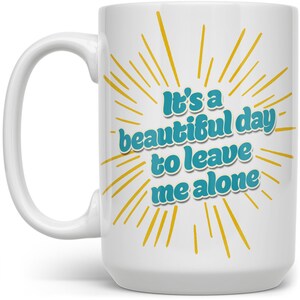 May include: White ceramic mug with a yellow sunburst design and the text "It's a beautiful day to leave me alone" in teal blue.