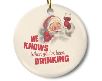 May include: Round ceramic Christmas ornament with a vintage illustration of Santa Claus winking and holding a glass of red wine. The text "HE KNOWS When you've been DRINKING" is printed in red.