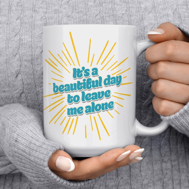 May include: White ceramic coffee mug with a blue and yellow design. The mug features the text "It's a beautiful day to leave me alone".