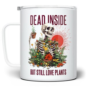 May include: White travel mug with a humorous design. The illustration features a skeleton with plants growing from its ribcage, holding a potted plant. Text reads "DEAD INSIDE BUT STILL LOVE PLANTS."