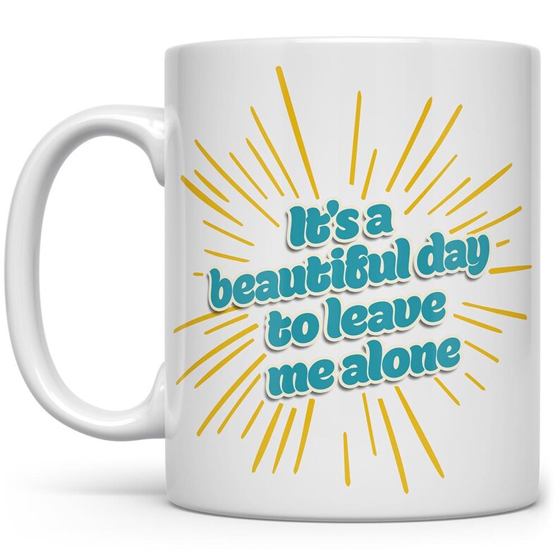 May include: White ceramic mug with a yellow sunburst design and the text "It's a beautiful day to leave me alone" in blue.